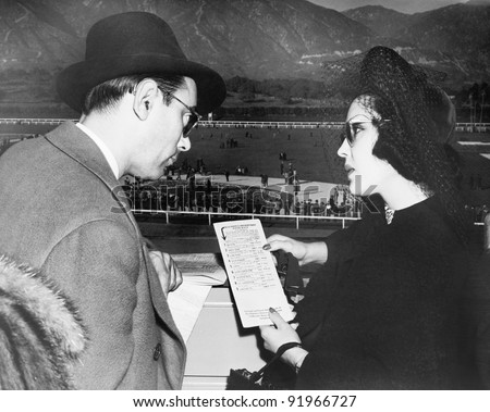 Elegant couple at a horse race looking at a program