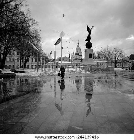 Kharkov, Ukraine - January 12, 2015: Reflection of an elderly woman with a cane and statues in a puddle on the marble pavement
