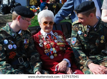 MOSCOW, RUSSIA - MAY 09: A war veteran woman and two young military men sit on a bench. Victory Day celebration on May 09, 2013 in Moscow.