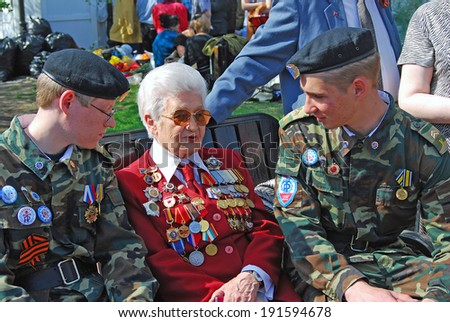 MOSCOW, RUSSIA - MAY 09: A war veteran woman sits on a bench together with two young military man, they are talking to each other. Victory Day celebration on May 09, 2013 in Moscow.