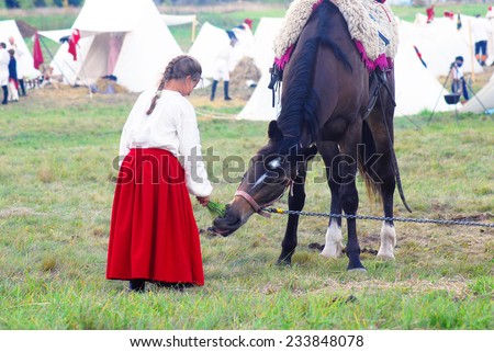 MOSCOW REGION - SEPTEMBER 07, 2014: Young reenactor feeds a horse with hay at a French camp. Borodino battle historical reenactment.