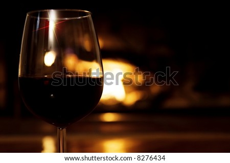 Glass of wine in front of the fireplace - horizontal.  Selective focus, golden glow from the fire.