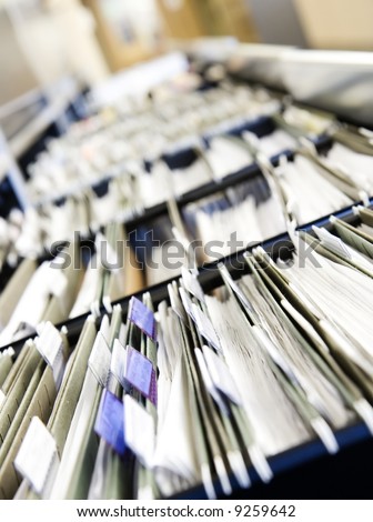 Multiple rows of filing cabinets in an office or medical establishment, overflowing with files.  Narrow depth of field to emphasize the \