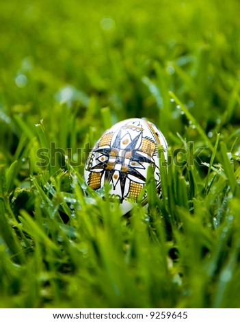 Traditional Easter Egg, painted with the symbol of the cross, on bright green grass covered with morning dew