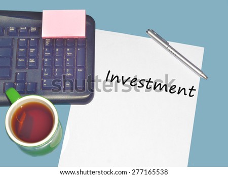 Keyboard with text INVESTMENT on table with tea, calculator and pen