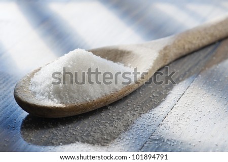 white sugar in wooden spoon on wooden table lighted by the sun