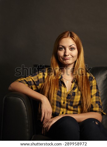 Attractive young woman with a funny grimace sitting on black sofa on black background