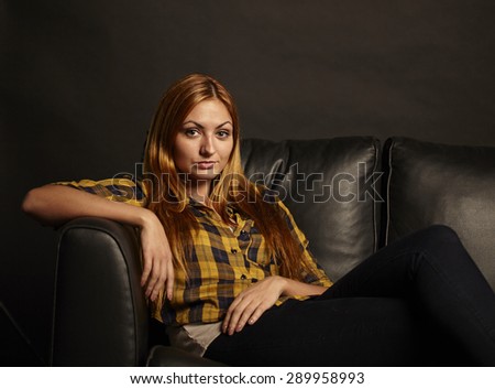 Attractive young woman with red hairs sitting on black sofa on black background