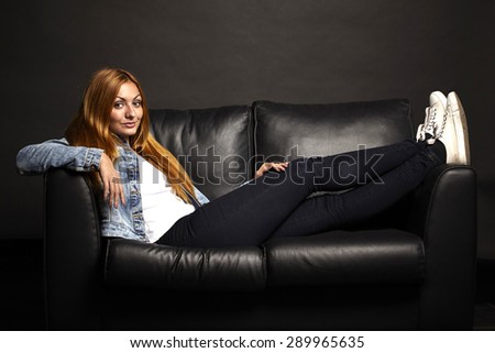 Attractive young woman with red hairs sitting on black sofa on black background
