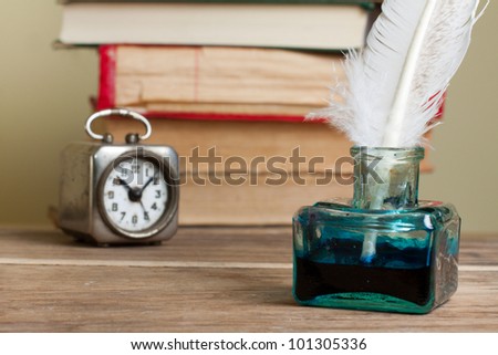 Quill and inkwell, old books, vintage clock on grunge wooden table