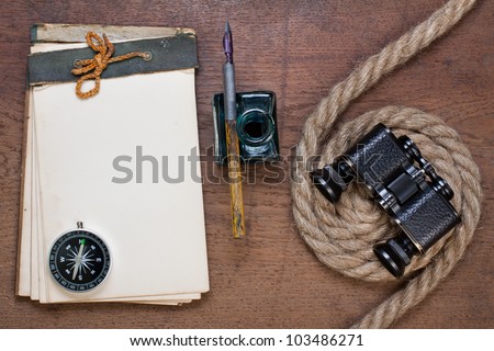 Antique notepad, compass, binoculars, ink pen, rope on the old wooden background