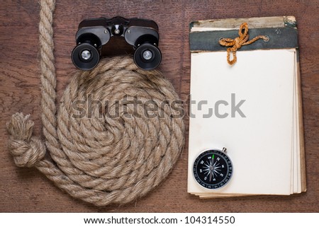 Old notebook, compass, binoculars, rope on the old wood background