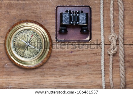 Big compass, binoculars and rope on wooden background