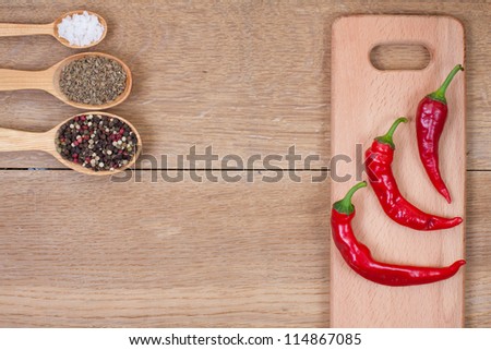 Red chili peppers,spices in spoons and kitchen board on oak wood texture background