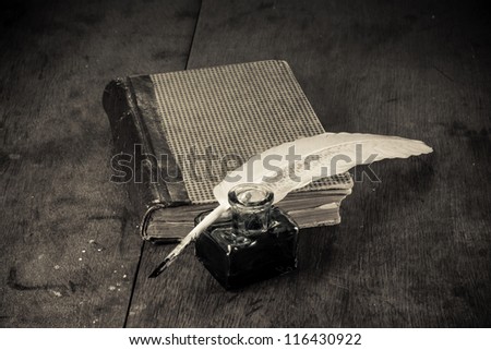 Quill and inkwell, book on old table background