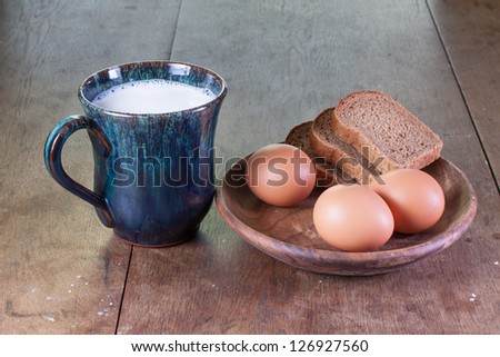 Eggs, bread, cup of milk on old oak table