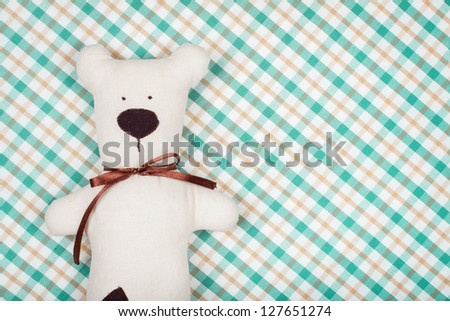 Handmade toy bear on checkered textile background