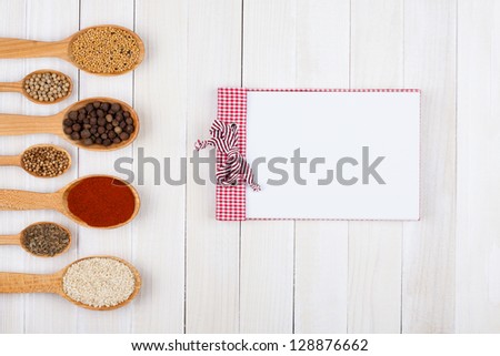 Recipe notepad, spices in wooden spoons on white wood background