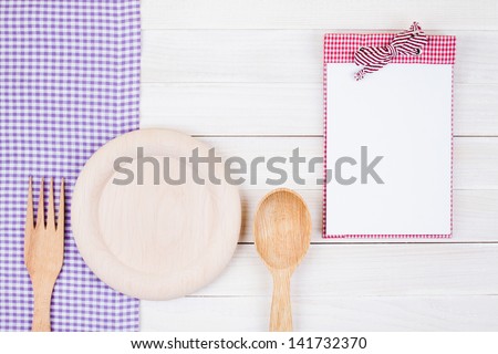 Menu or recipe book, plate, spoon, fork, tablecloth on white wood background
