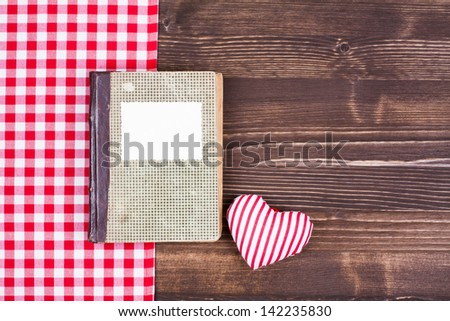 Old cook book with heart, tablecloth on wooden table background