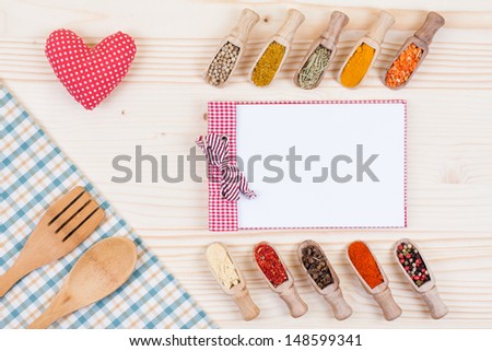 Spices in scoops, recipe cook book, spoon, fork, tablecloth textile, heart on wood background