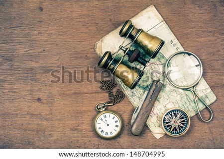 Vintage binoculars, compass, old map, magnifying glass, pocket watches, knife on wooden background