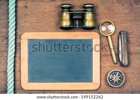 Chalk board, binoculars, compass, magnifying glass, knife, rope on wooden background