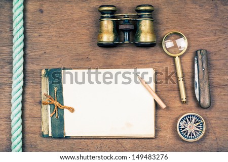 Vintage notebook, compass, binoculars, old pocket knife, pencil, magnifying glass on wooden background