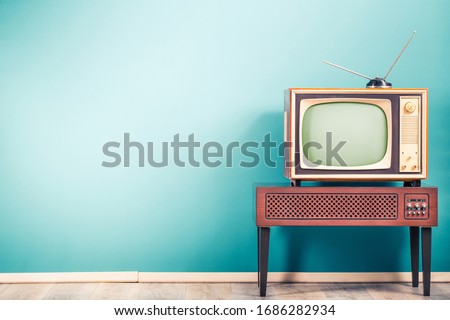 Retro old outdated classic television receiver with TV antenna from circa 60s of XX century on wooden stand with amplifier front gradient mint blue wall background. Vintage style filtered photo