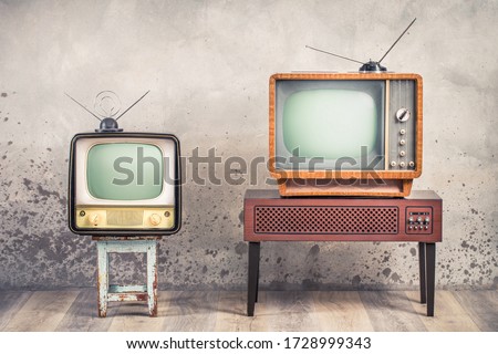 Two old retro classic analog CRT TV set receivers and aged wooden television stand with outdated amplifier front aged concrete wall background. Broadcasting, news concept. Vintage style filtered photo