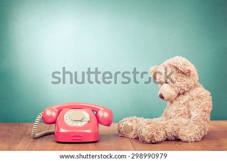 Retro rotary telephone and old Teddy Bear front mint green wall background. Vintage instagram style filtered photo