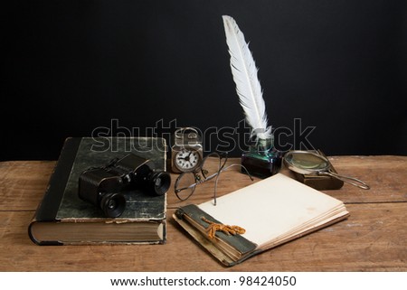 Antique book, binoculars, quill ink pen and inkwell, magnifying glass, old notepad, vintage clock, spectacles on wood table
