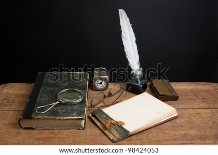 Quill ink pen and inkwell, antique book, magnifying glass, old notepad, vintage clock, spectacles on wood table