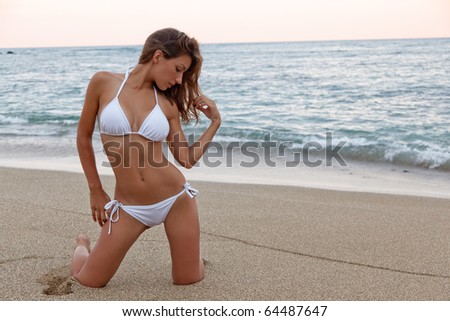 A Woman in a white bikini poses while ont he beach