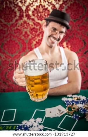 Mustache man in glasses, hat, and mustache smiling while toasting with large glass of beer at retro red casino blackjack table wearing white tank top
