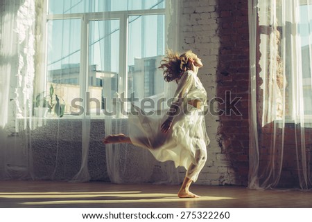 Beautiful woman in light interior with big windows listening music and dancing. Home comfort concept