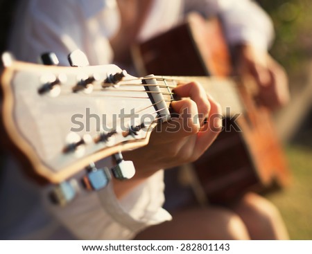 Young woman in sun park holding a guitar and playing music