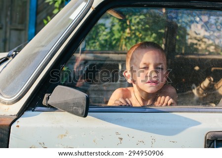 Funny little boy pressed against the glass in old car and thinking