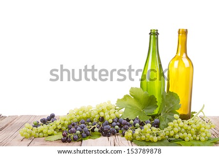 grapes on vine with leaves with empty wine bottles sitting on wooden plank with an isolated white background