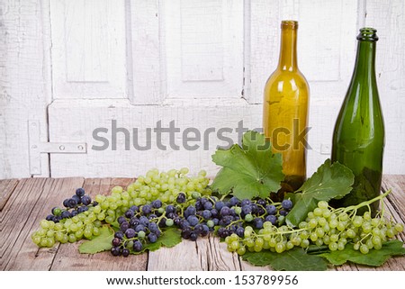 grapes on vine with leaves and empty wine bottles on wooden plank