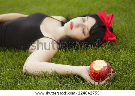 Young girl laying on grass holding a poison apple