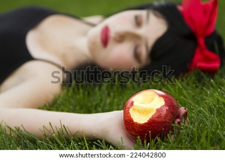 Young girl laying on grass holding a poison apple