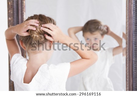 Child or young girl fixing her hair while looking in the mirror.