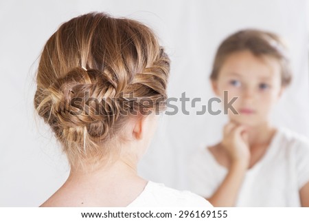 Child or young girl staring at herself in a mirror, with a fish tail braid in her hair.