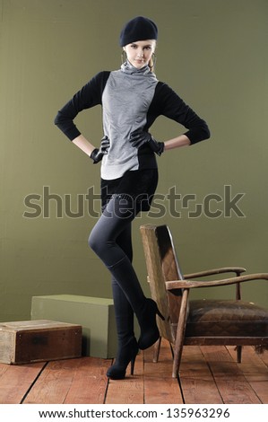 Full length young woman posing near chair with cube on wooden floor