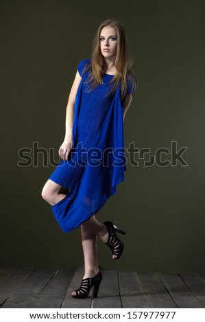 Full length portrait of young woman in blue dress posing wooden floor