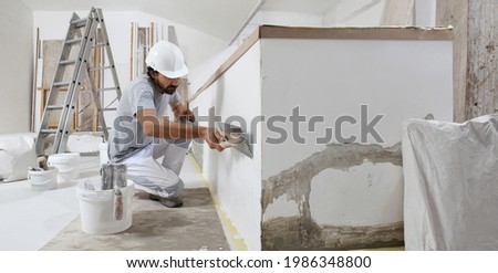 man plasterer construction worker at work, takes plaster from bucket and puts it on trowel to plastering the wall, wears helmet inside the building site of a house Photo stock © 