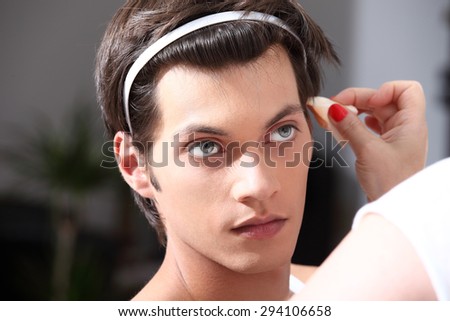 makeup artist applying foundation with a brush, man in the dressing room mirror
