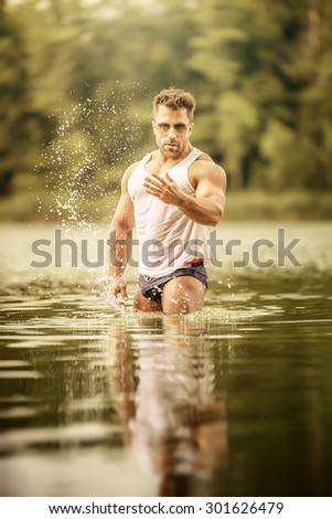 An image of a muscular man in the lake with a white shirt and sunglasses
