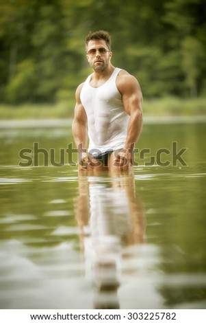 An image of a muscular man in the lake with a white shirt and sunglasses